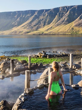 Person enjoying Hvammsvik Hot Spring with scenic mountain backdrop in Iceland.