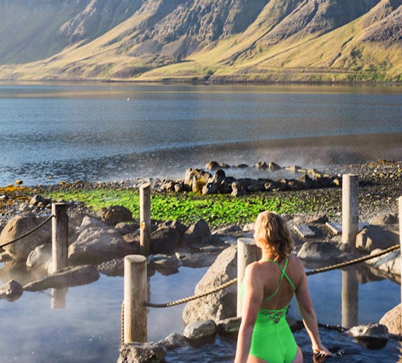 Person enjoying Hvammsvik Hot Spring with scenic mountain backdrop in Iceland.