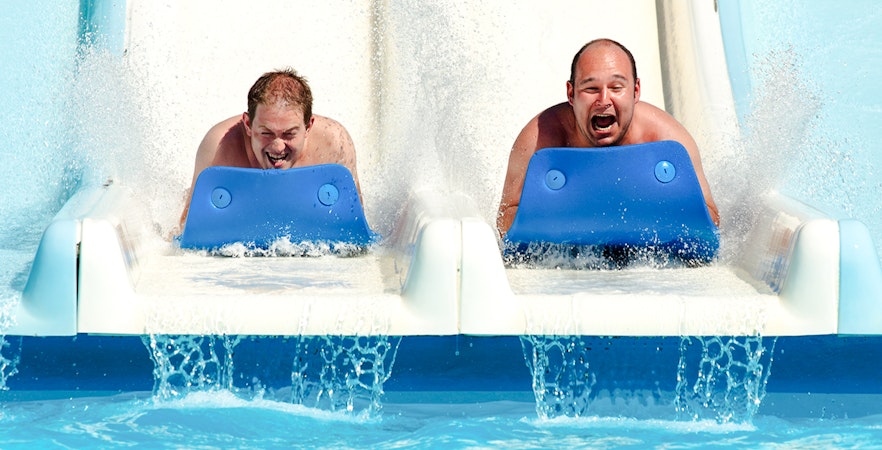 Two people sliding down a water slide on mats at a water park.