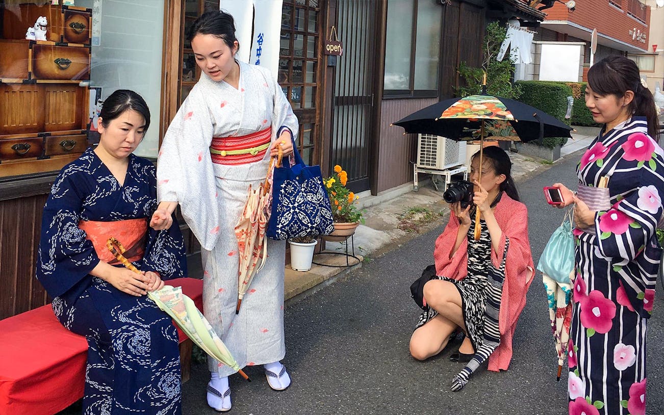 Women in traditional kimonos during a cultural experience in Japan, one holding a camera.
