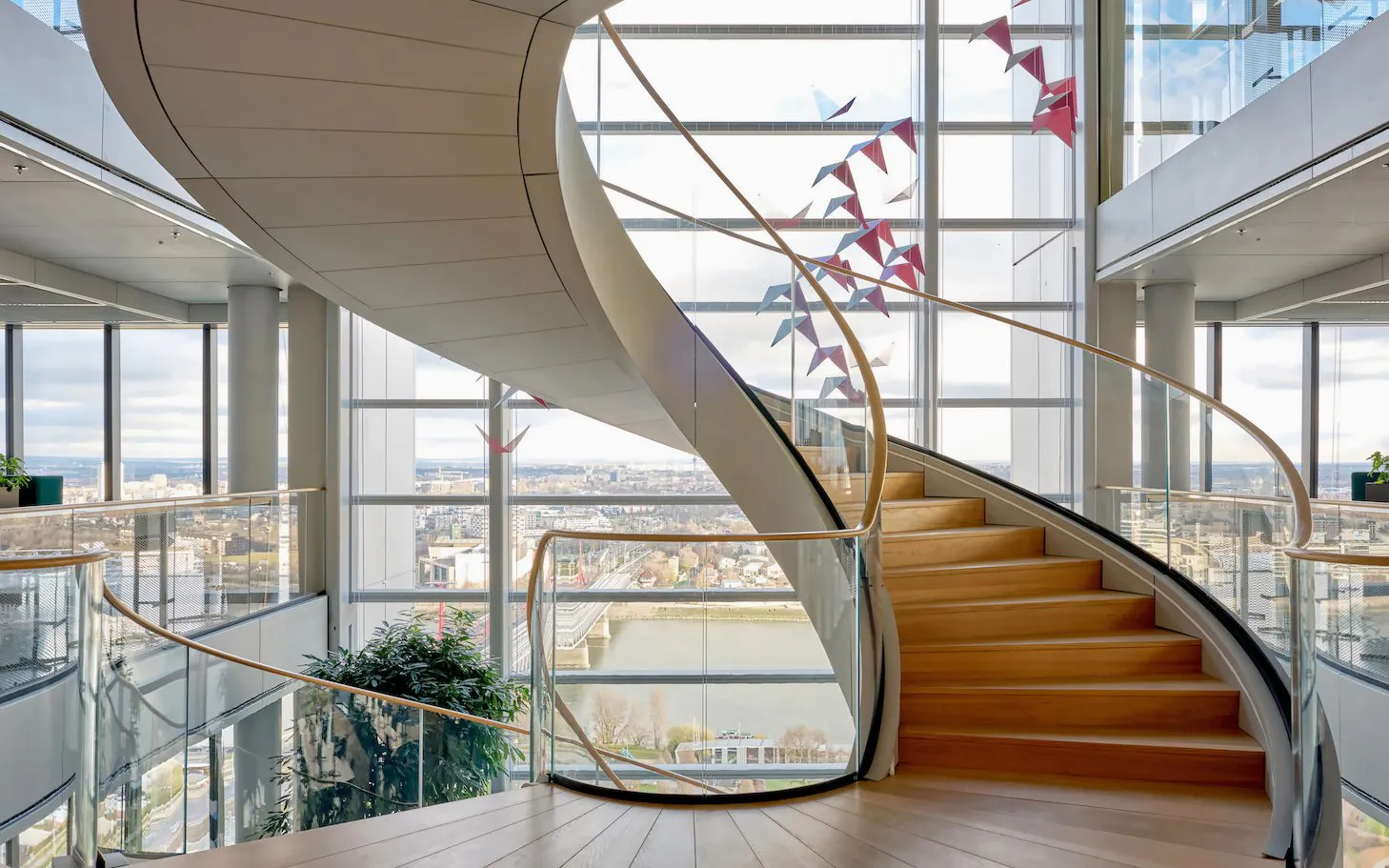 Spiral staircase at SkyDeck, MOL Campus, Budapest with city view through large windows.