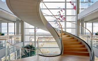 Spiral staircase at SkyDeck, MOL Campus, Budapest with city view through large windows.