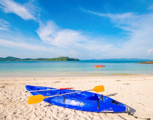 Blue kayaks on the sandy shore of Koh Naka Noi Beach, Phuket, with Naka Island in the background.