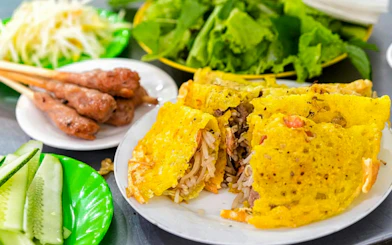 Vietnamese savory pancakes with crispy yellow shell, served with fresh greens and skewered meat.