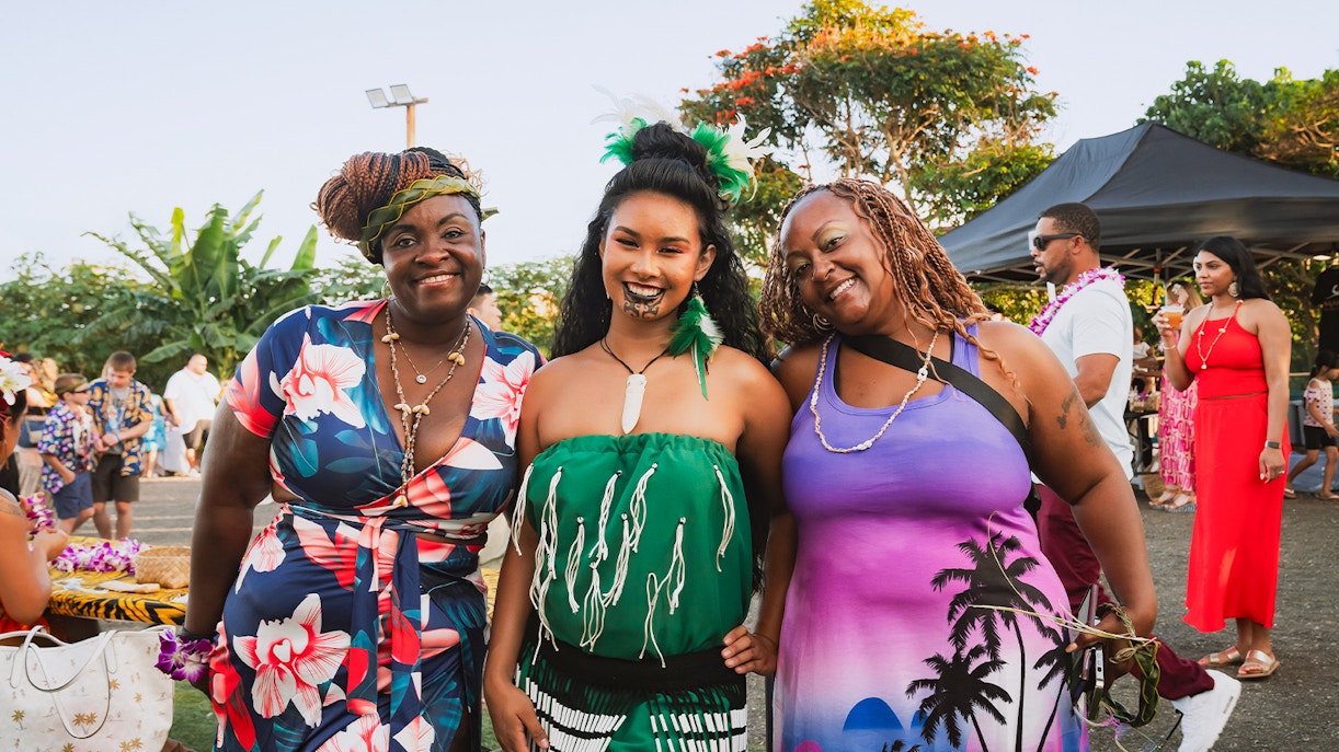 Guests with a Polynesian woman in traditional attire at Mauka Warriors Luau.