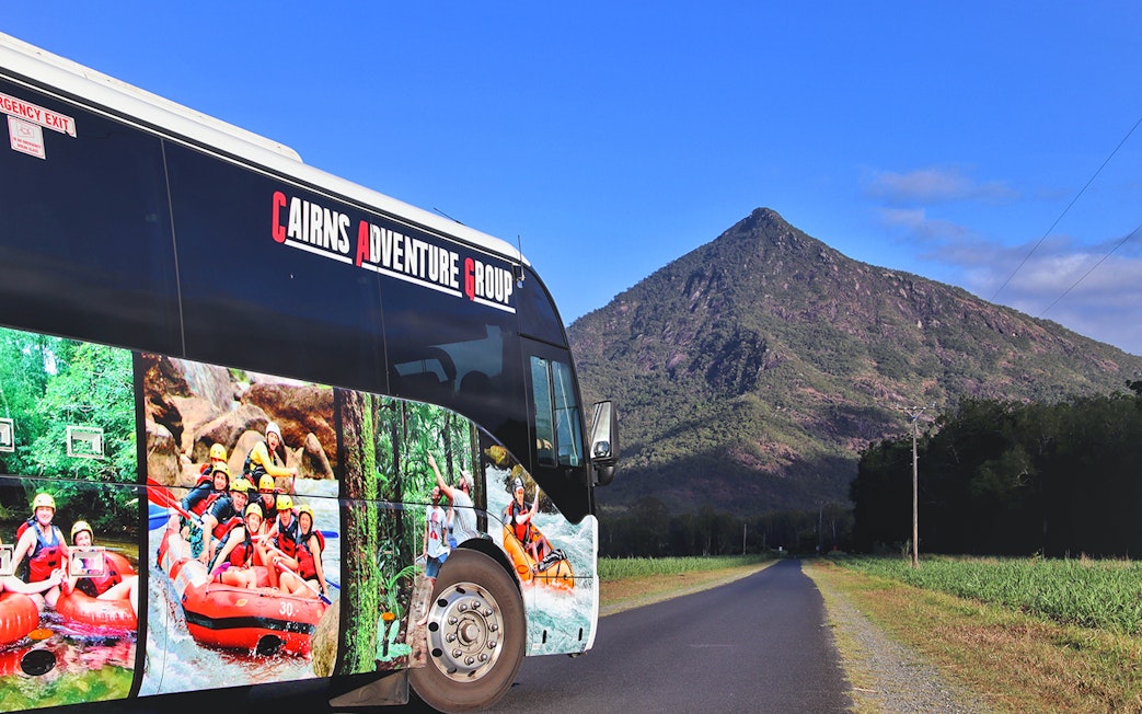 Tour bus with rafting images parked near a mountain on the way to Tully River.