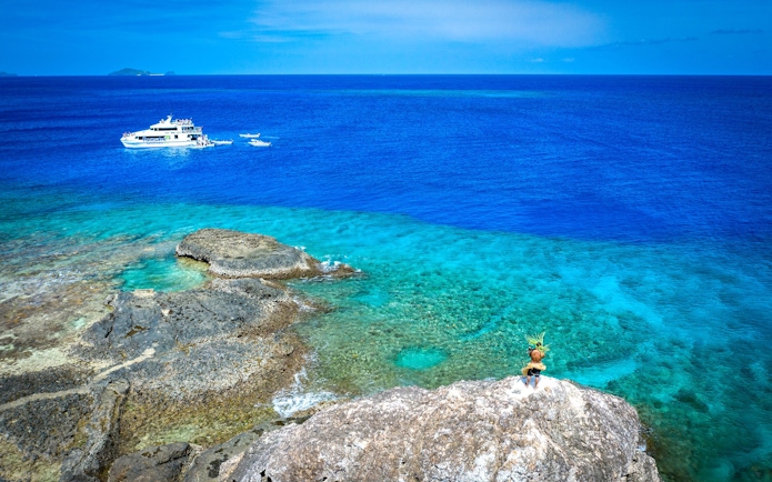 Cruise ship in blue waters near Kuata Island, Fiji with rocky shoreline.