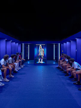 Visitors seated in a blue-lit room viewing a display of a football player at The Messi Experience Dubai.
