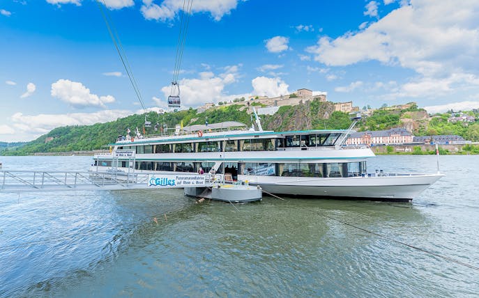 Koblenz sightseeing cruise boat on the Rhine River with Ehrenbreitstein Fortress in the background.