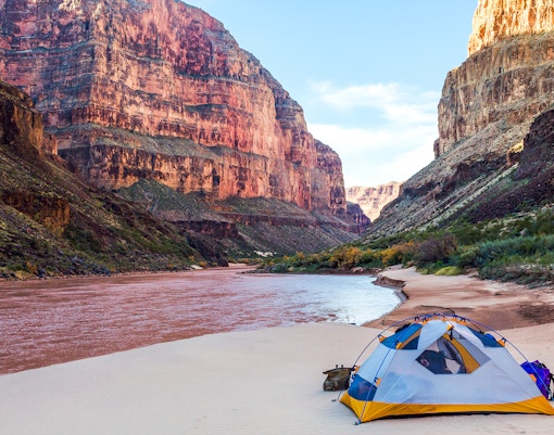Camping tent by the river in Grand Canyon National Park with towering canyon walls.