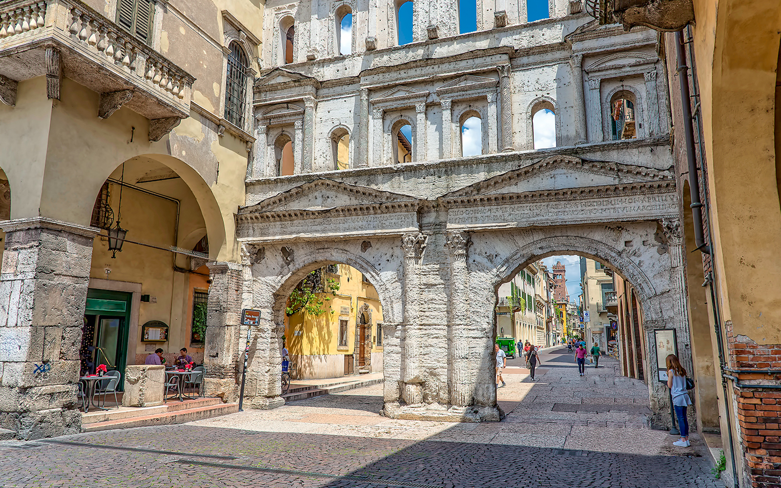 Verona street scene with ancient Roman archway and people walking.