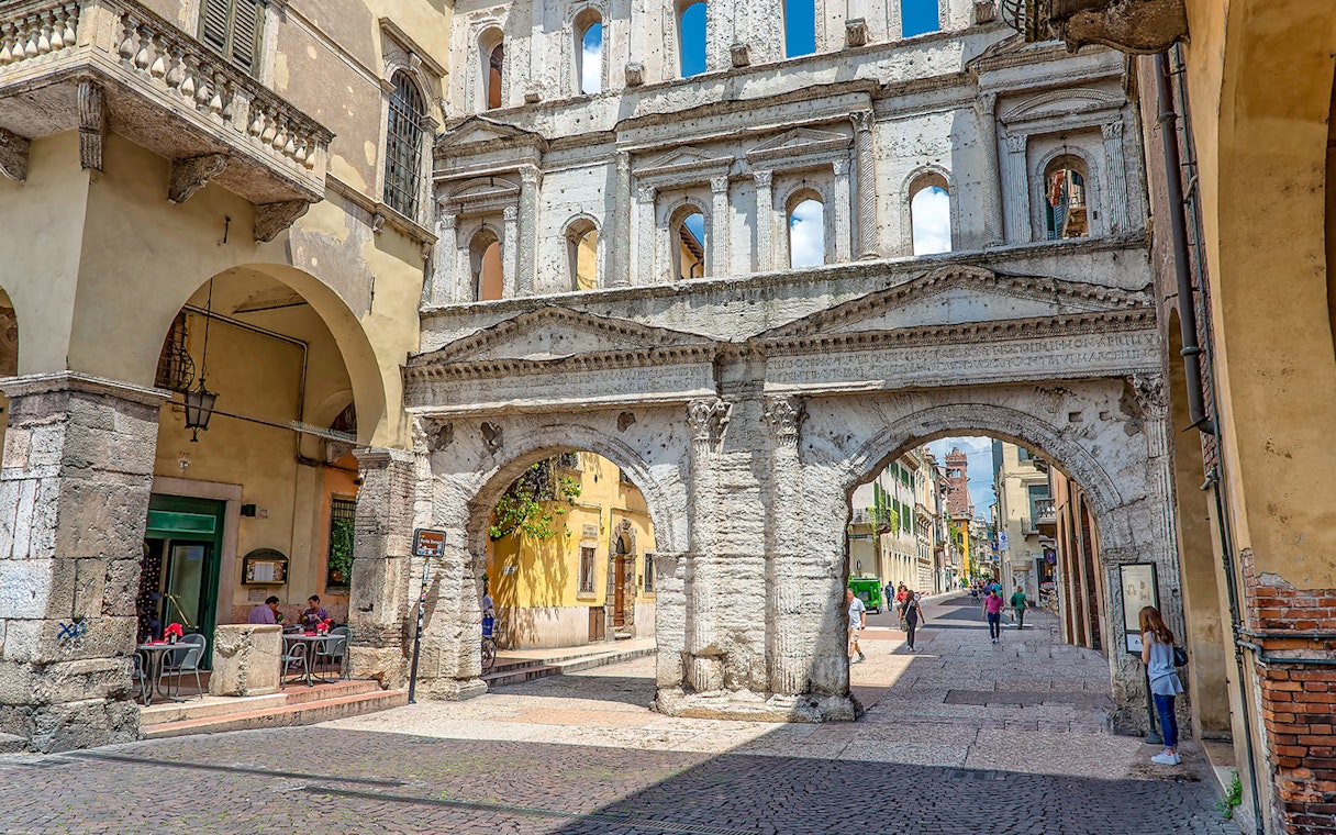 Verona street scene with ancient Roman archway and people walking.