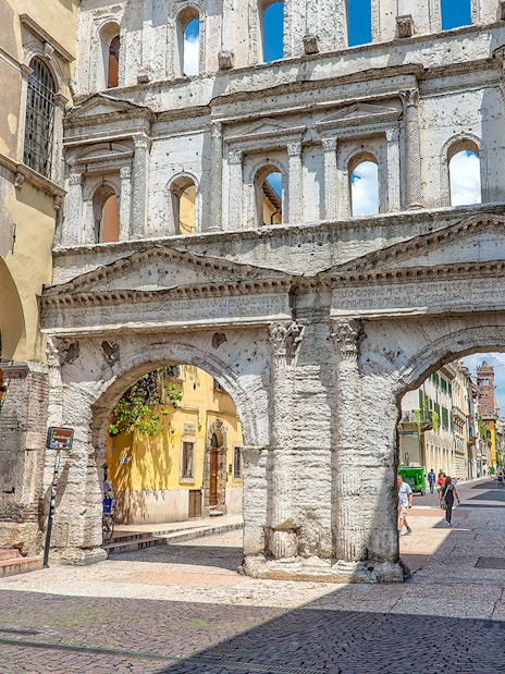 Verona street scene with ancient Roman archway and people walking.