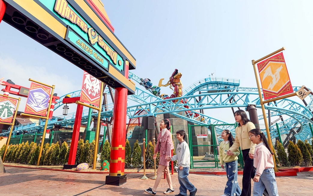 Visitors entering the Master Spinjitzu ride at Legoland with roller coaster in background.