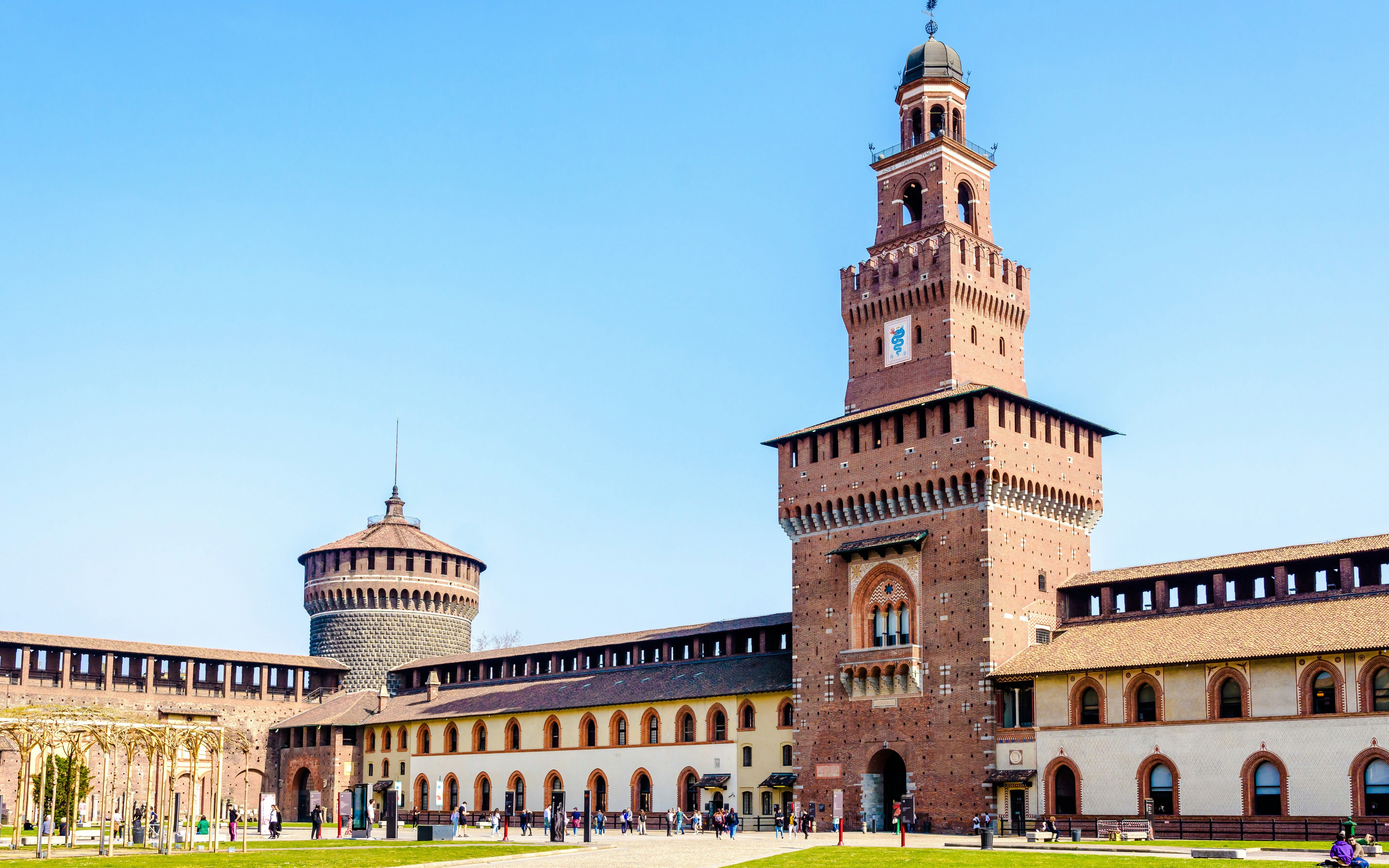 Torre del Filarete at Castello Sforzesco, Milan, with tourists exploring the courtyard.