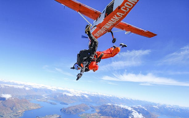 Tandem skydivers freefalling over Lake Wanaka, New Zealand, with mountains in the background.