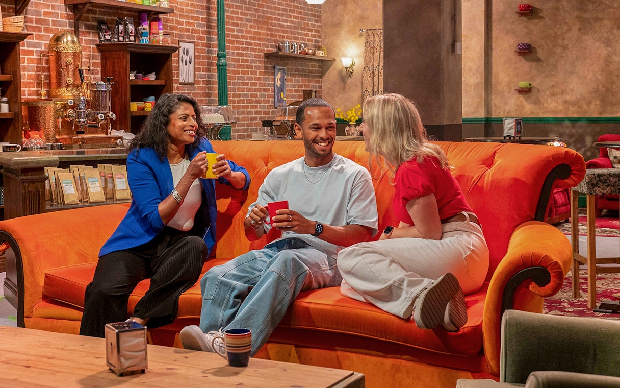 Visitors enjoying coffee on the iconic orange couch at The FRIENDS™ Experience.