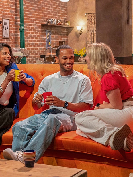Visitors enjoying coffee on the iconic orange couch at The FRIENDS™ Experience.