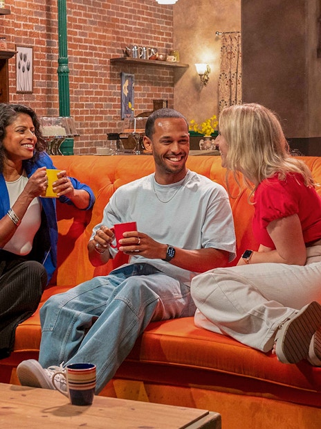 Visitors enjoying coffee on the iconic orange couch at The FRIENDS™ Experience.