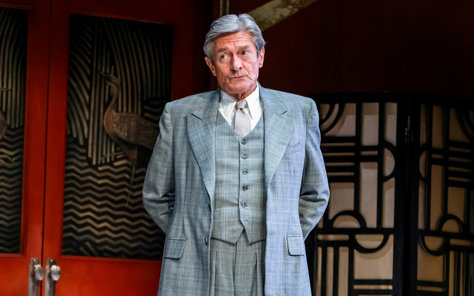 Man in a gray suit standing in front of an art deco backdrop during "Private Lives" performance.