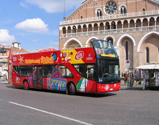 Red double-decker tour bus in front of historic building in Padua, Italy.