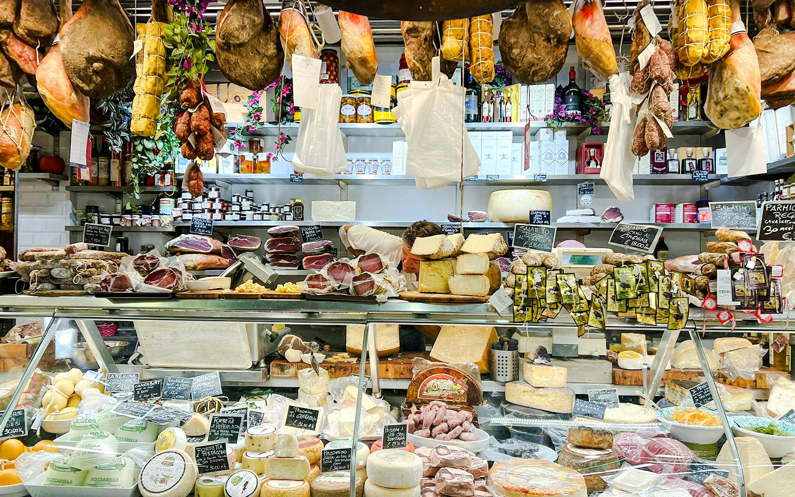 Florence deli with hanging cured meats and cheese display for cooking class.