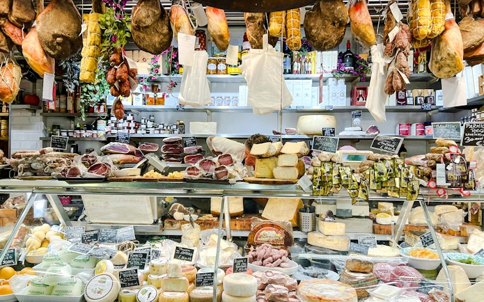 Florence deli with hanging cured meats and cheese display for cooking class.