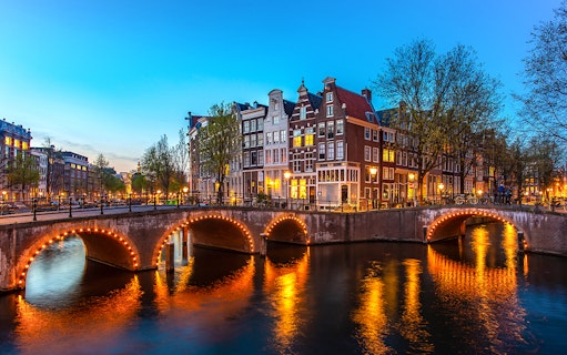 Amsterdam canal bridge illuminated at night with historic buildings in the background.