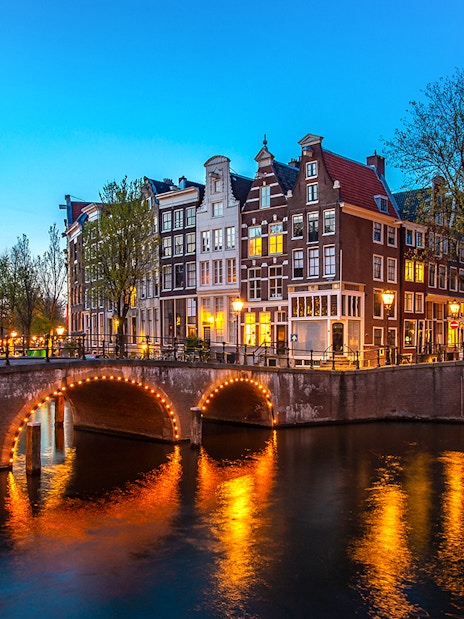 Amsterdam canal bridge illuminated at night with historic buildings in the background.