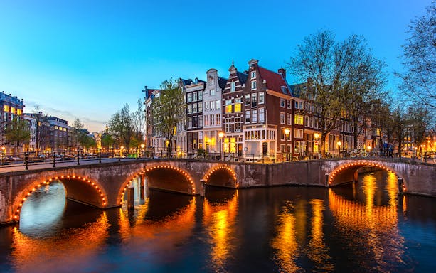 Amsterdam canal bridge illuminated at night with historic buildings in the background.
