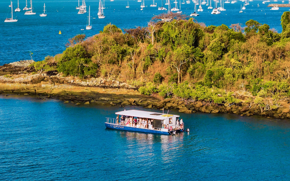 Aerial view of a sundowner cruise near lush island, Airlie Beach, with sailboats in the background.