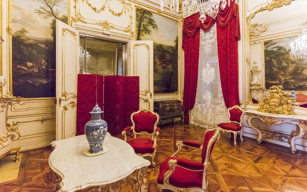 Schönbrunn Palace interior with ornate red chairs, marble table, and decorative vase.