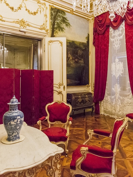 Schönbrunn Palace interior with ornate red chairs, marble table, and decorative vase.