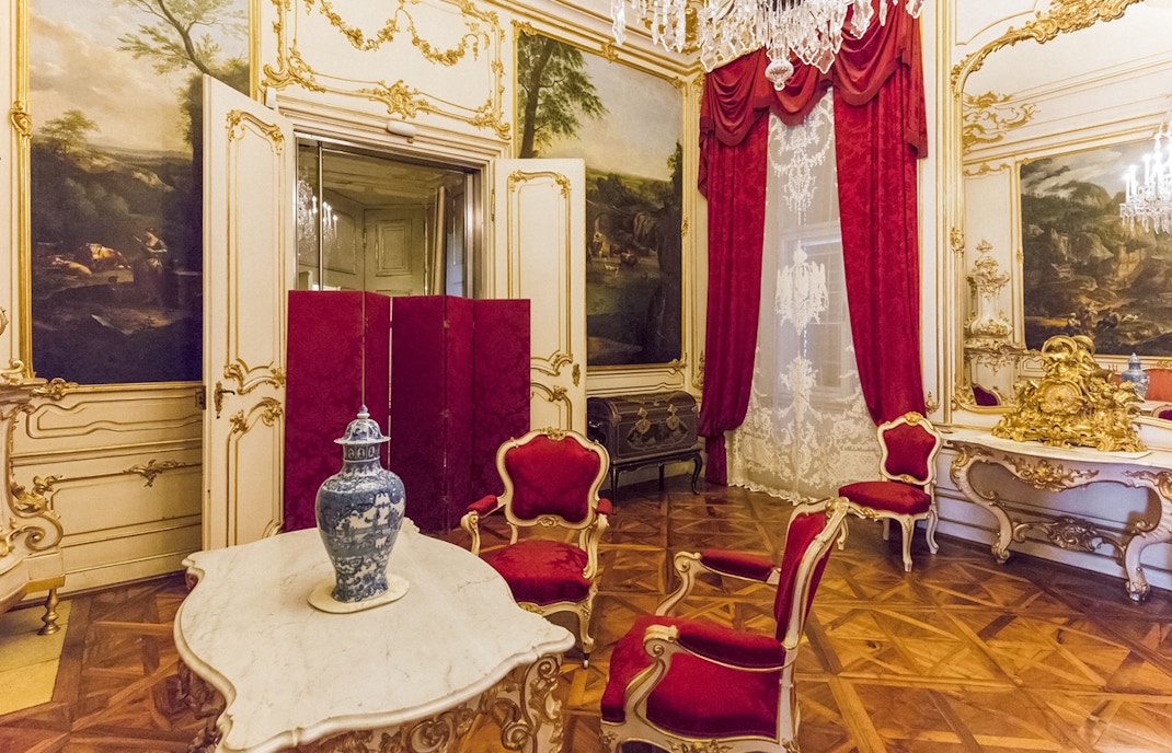 Schönbrunn Palace interior with ornate red chairs, marble table, and decorative vase.