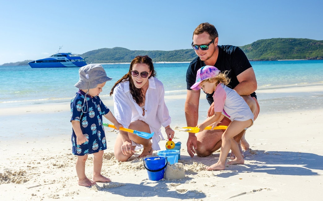Family playing on Airlie Beach with a boat in the background.