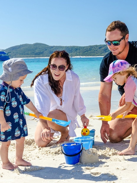 Family playing on Airlie Beach with a boat in the background.