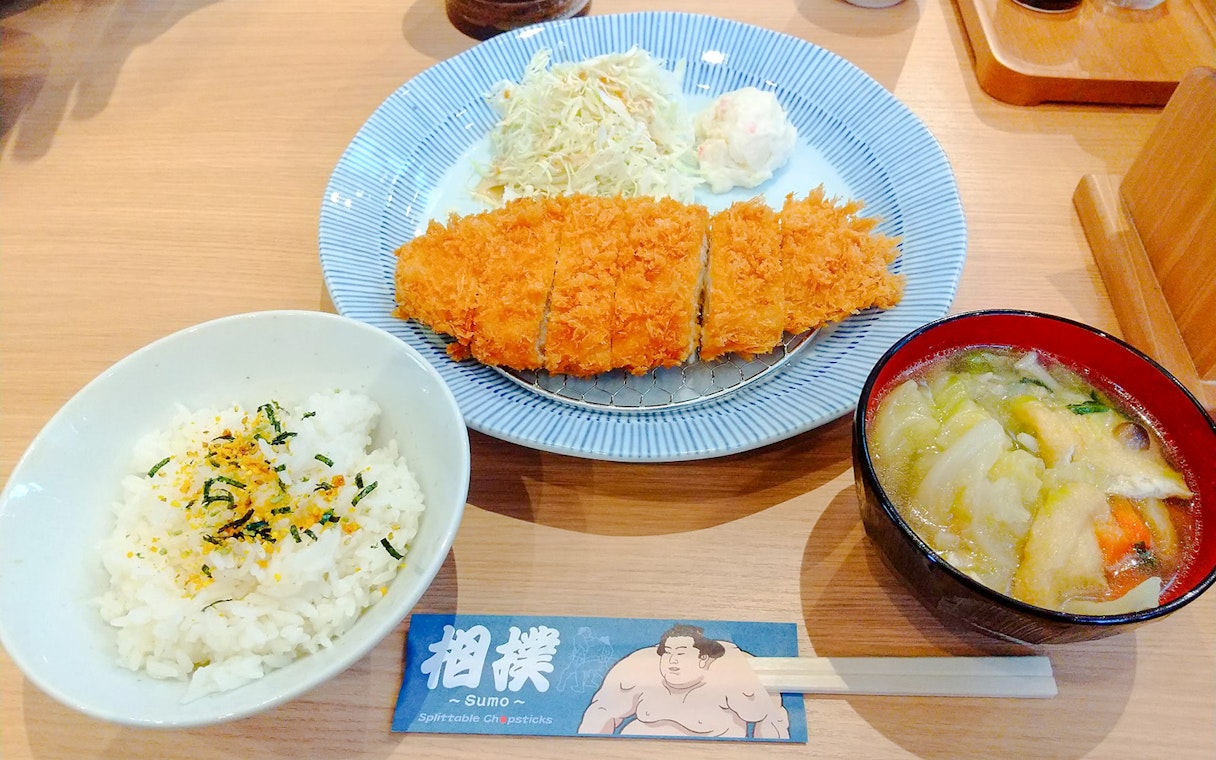 Sumo show lunch with rice, miso soup, and breaded cutlet on a plate.