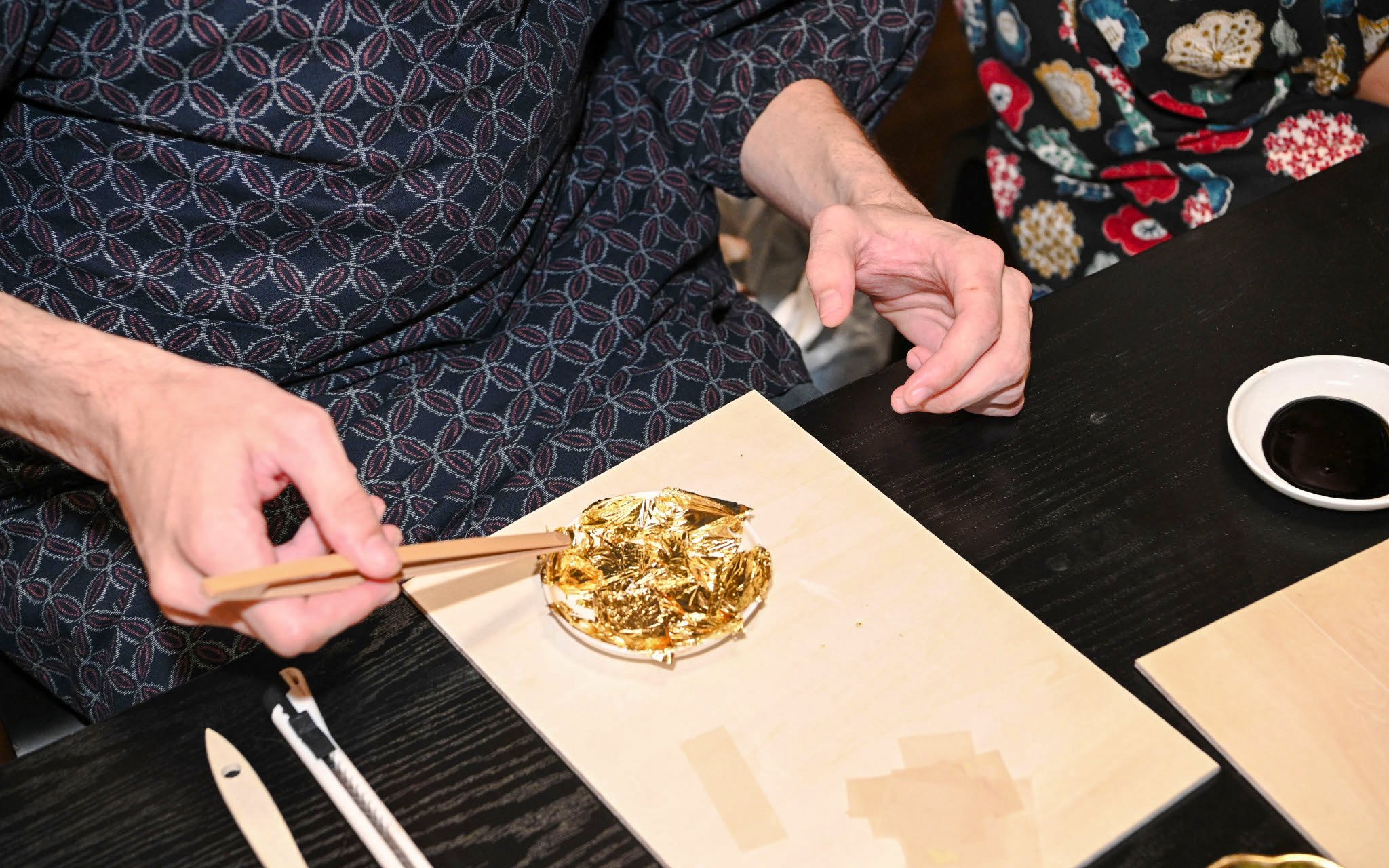 Hands applying gold leaf with tweezers during a gold plating workshop.