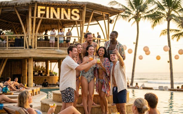 Tourists enjoying a party at Finn's Beach Club with drinks and a sunset view.