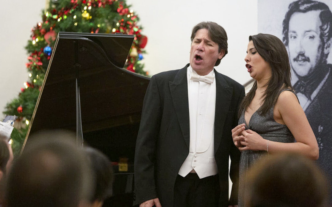 Opera singers performing at a Christmas concert with a decorated tree in the background.