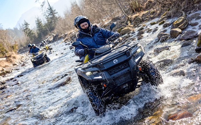 Quad biking through a rocky stream in Zakopane with riders wearing helmets and winter gear.