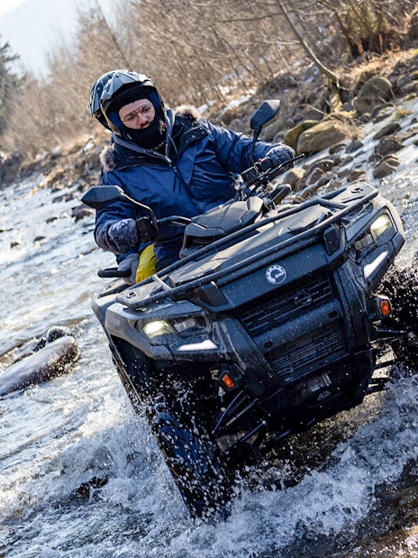 Quad biking through a rocky stream in Zakopane with riders wearing helmets and winter gear.