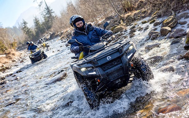 Quad biking through a rocky stream in Zakopane with riders wearing helmets and winter gear.