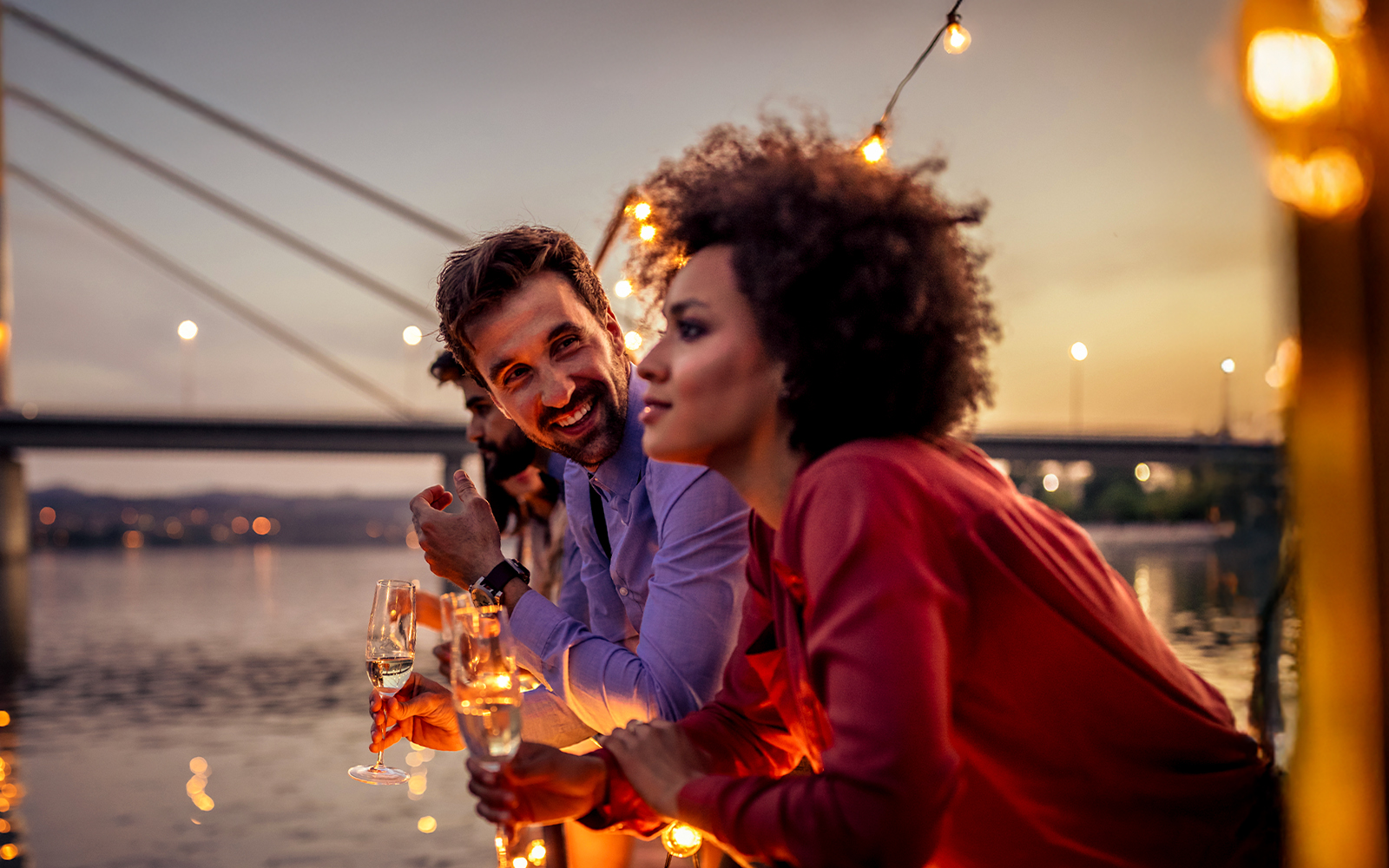 Tourists enjoying sunset view on Douro River party cruise with bridge in background.