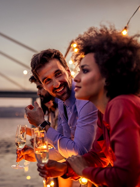 Tourists enjoying sunset view on Douro River party cruise with bridge in background.