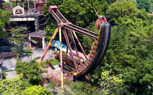 Pirate ship ride swinging at Sunway Lagoon Theme Park amidst lush greenery.