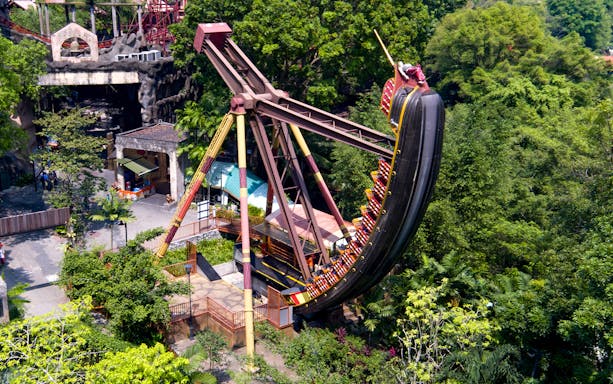 Pirate ship ride swinging at Sunway Lagoon Theme Park amidst lush greenery.