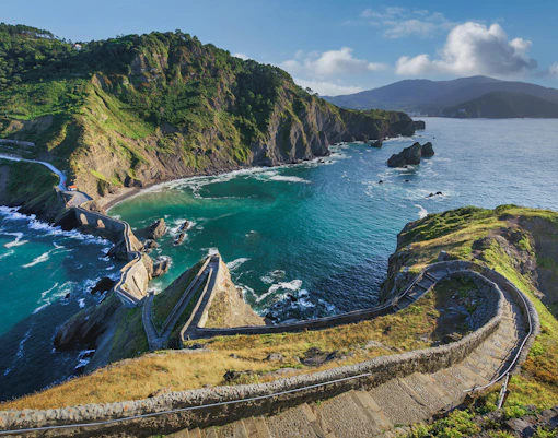 Winding stone staircase descending to coastal bay with turquoise waters and rocky cliffs, San Juan de Gaztelugatxe, Spain.