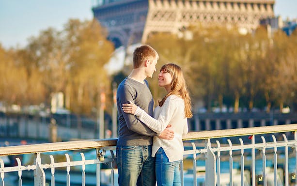 Couple embracing on a Paris bridge with Eiffel Tower in background.