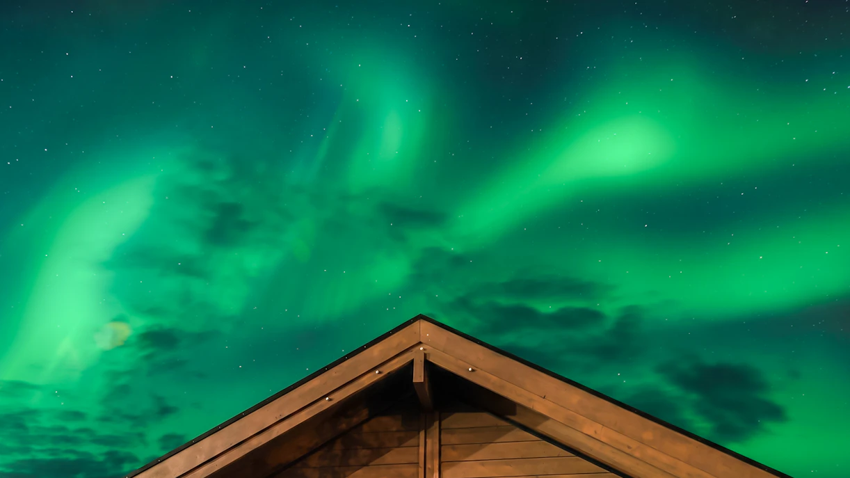Aurora Borealis over lodge roof, Northern Lights Alaska.